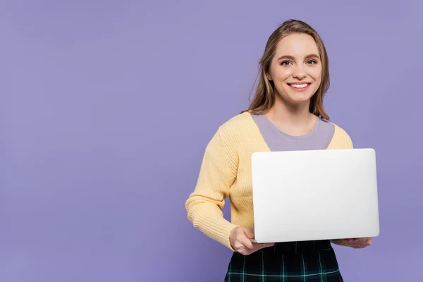 Alegre joven mujer sosteniendo portátil aislado en púrpura - foto de stock