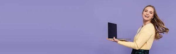 Cheerful young woman holding laptop with blank screen isolated on purple, banner — Stock Photo