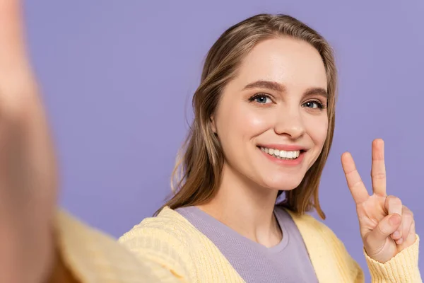 Fröhliche junge Frau zeigt Friedenszeichen isoliert auf lila — Stockfoto