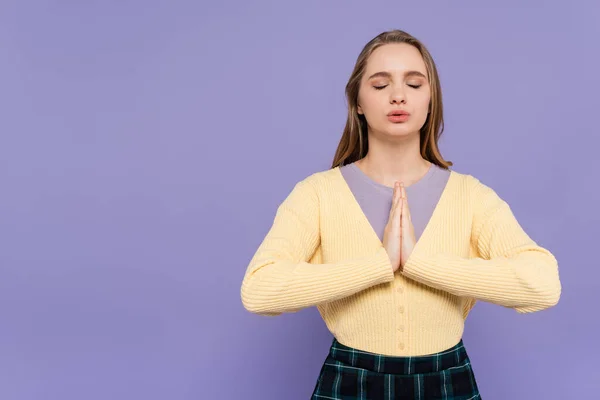 Mujer joven con los ojos cerrados y las manos de oración aisladas en púrpura - foto de stock