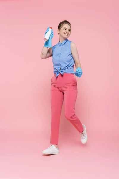 Comprimento total da jovem mulher feliz em luvas de borracha segurando garrafa ambientador de ar em rosa — Fotografia de Stock