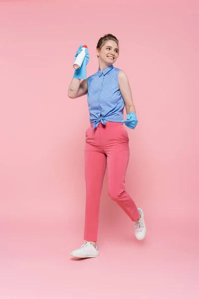 Pleine longueur de jeune femme heureuse dans des gants en caoutchouc tenant bouteille de désodorisant sur rose — Photo de stock