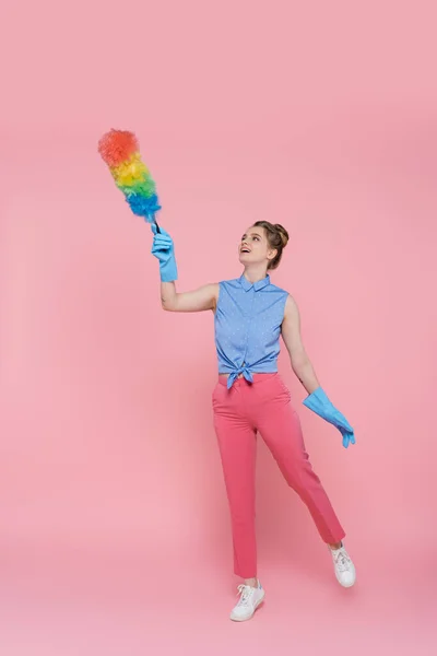 Full length of tattooed young woman in blue rubber gloves holding dust brush on pink — Stock Photo