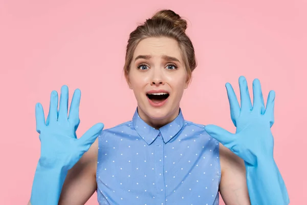 Mujer sorprendida mostrando las manos en guantes de goma azul aislados en rosa - foto de stock