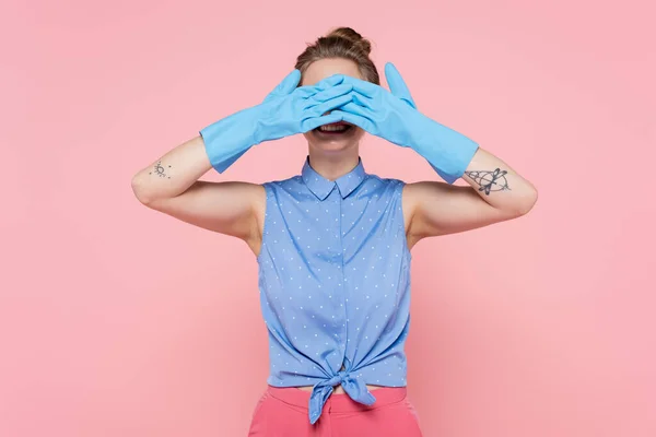 Mujer joven tatuada sonriendo y cubriendo los ojos aislados en rosa - foto de stock