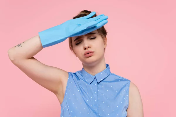 Tired and tattooed young woman in rubber glove wiping sweat isolated on pink — Stock Photo