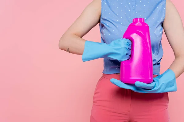 Vista recortada de mujer tatuada en guantes de goma sosteniendo botella brillante con detergente aislado en rosa - foto de stock