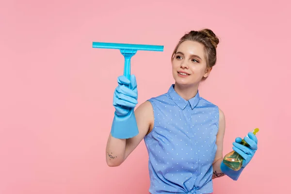 Joyeuse jeune femme en gants de caoutchouc tenant essuie-glace et vaporisateur isolé sur rose — Photo de stock