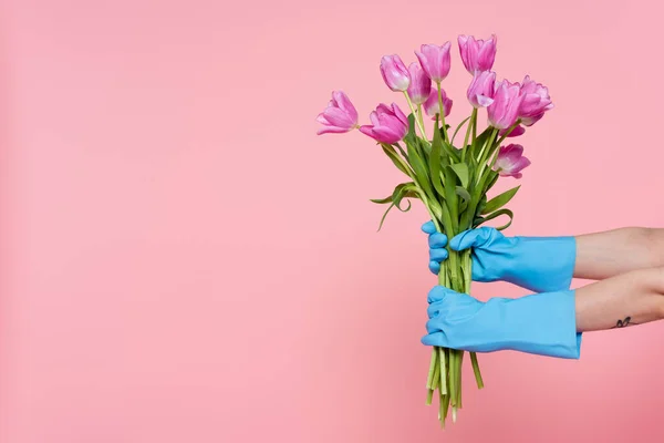 Vista recortada de la mujer en guantes de goma con tulipanes aislados en rosa, concepto de limpieza de primavera - foto de stock