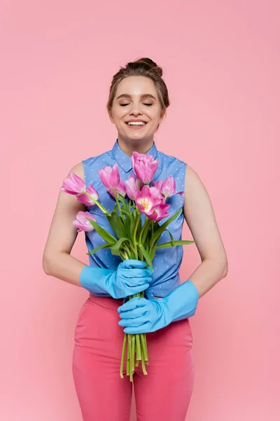 Jovem feliz em luvas de borracha segurando tulipas isoladas em rosa — Fotografia de Stock