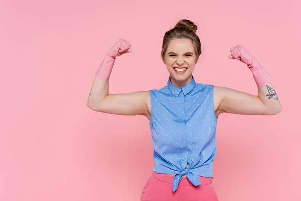 Happy and tattooed woman in rubber gloves showing power isolated on pink — Stock Photo