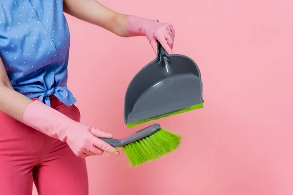 Vista recortada de mujer joven en guantes de goma con escoba y recogedor aislado en rosa - foto de stock