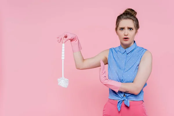 Jeune femme tatouée dans des gants en caoutchouc tenant brosse de toilette isolée sur rose — Photo de stock