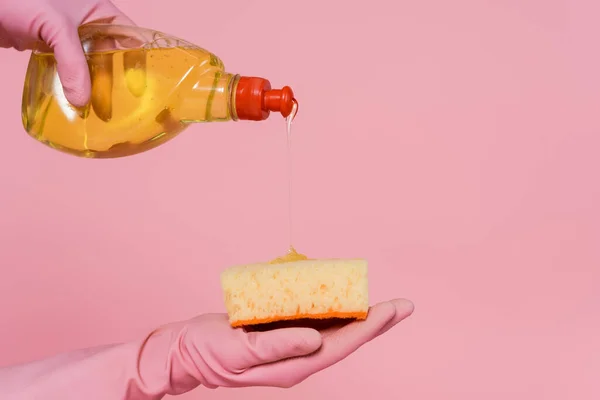 Vista parcial de la mujer vertiendo detergente sobre la esponja aislado en rosa - foto de stock