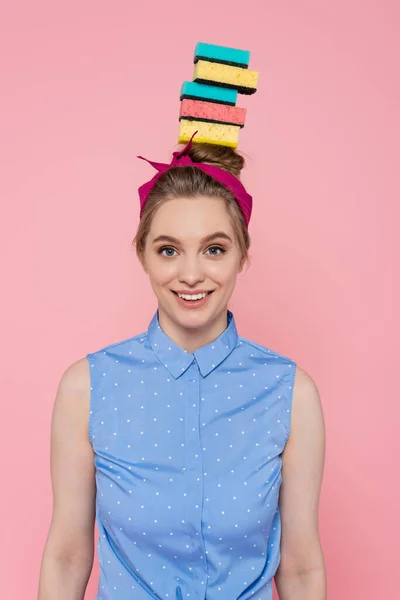 Glückliche junge Frau mit gestapelten Schwämmen auf dem Kopf isoliert auf rosa — Stockfoto