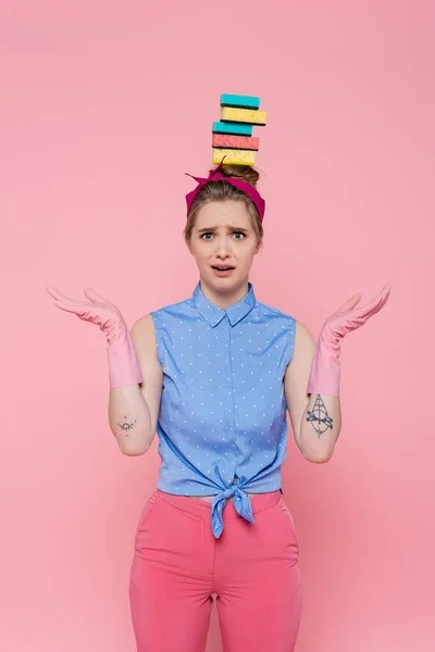 Confused young woman with stacked sponges on head isolated on pink — Stock Photo