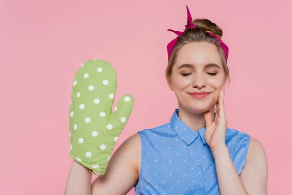 Pleased young woman with green baking glove isolated on pink — Stock Photo