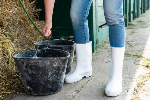 Cropped view of farmer in white rubber boots near buckets and hay — Stock Photo