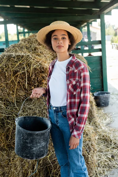 African american farmer with bucket looking at camera near haystack — Stock Photo