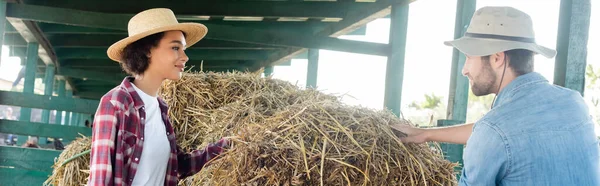 Fermiers interracial souriant à l'autre près de la botte de foin à la ferme, bannière — Photo de stock