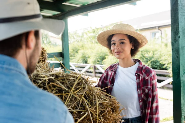 Positive african american woman looking at blurred farmer near haystack — Stock Photo