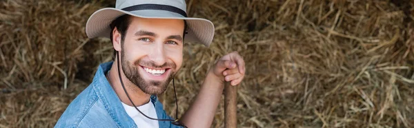 Giovane agricoltore in cappello tesa sorridente alla fotocamera vicino pagliaio, banner — Foto stock