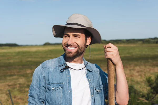 Agricultor sorrindo olhando para longe, enquanto em pé no prado — Fotografia de Stock