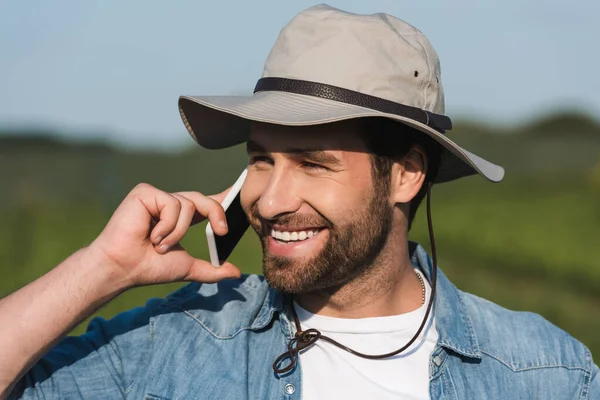 Joyful farmer in brim hat talking on mobile phone and looking away outdoors — Stock Photo