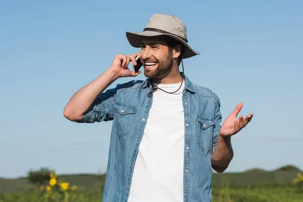 Cheerful farmer in brim hat talking on cellphone outdoors — Stock Photo