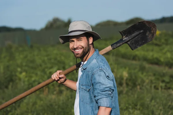 Farmer in brim hat smiling at camera while holding shovel — Stock Photo