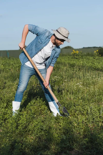 Piena lunghezza vista del contadino in cappello tesa e denim vestiti scavare nel campo — Foto stock