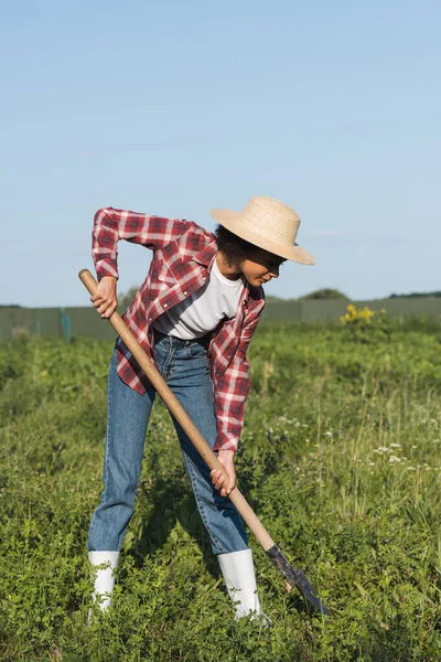 Full length view of african american woman in straw hat digging in field — Stock Photo