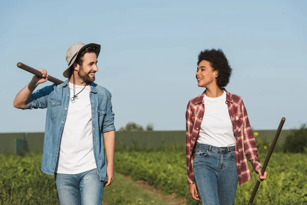 Jóvenes agricultores interraciales sonriéndose unos a otros en el campo verde - foto de stock