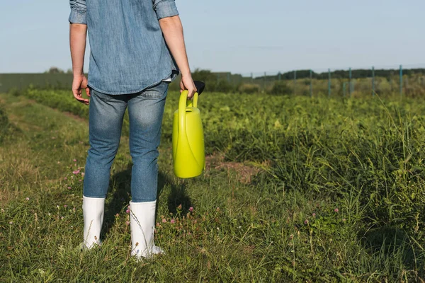 Partial view of farmer in white rubber boots standing with yellow watering can in field — Stock Photo