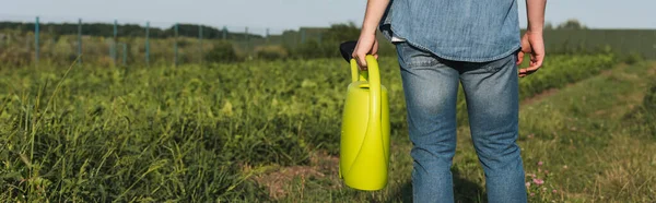 Cropped view of farmer in denim clothes standing with watering can in field, banner — Stock Photo