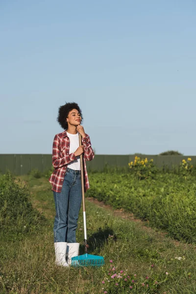 Vue complète de la femme afro-américaine avec des râteaux regardant loin dans le champ — Photo de stock
