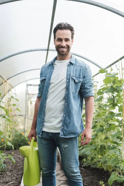 Jovem agricultor com rega pode sorrir para a câmera em estufa — Fotografia de Stock