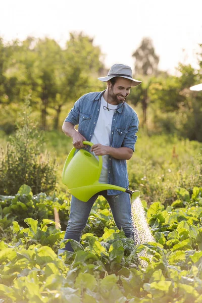 Smiling farmer in brim hat and denim clothes watering plants in garden — Stock Photo