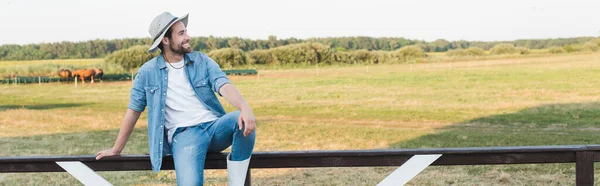 Zufriedener Bauer mit Krempe sitzt auf Holzzaun im Feld, Transparent — Stockfoto