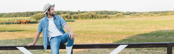 Pleased farmer in brim hat sitting on wooden fence in field, banner — Stock Photo