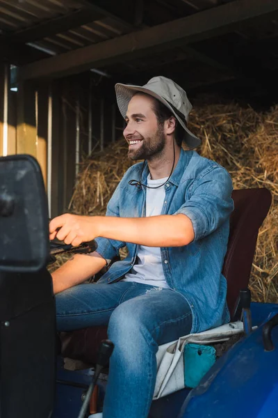 Glücklicher Bauer mit Krempe, der auf Traktor sitzt und wegschaut — Stockfoto