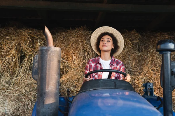 Mujer afroamericana mirando hacia otro lado mientras conduce tractor en granja - foto de stock