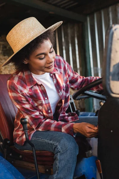 Young african american woman in straw hat starting tractor on farm — Stock Photo