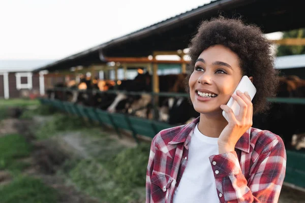 Allegra donna afroamericana distogliendo lo sguardo mentre parla su smartphone in fattoria — Foto stock
