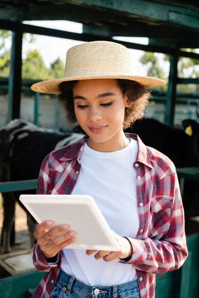 Jeune femme afro-américaine en chapeau de paille en utilisant une tablette numérique près d'étable floue — Photo de stock