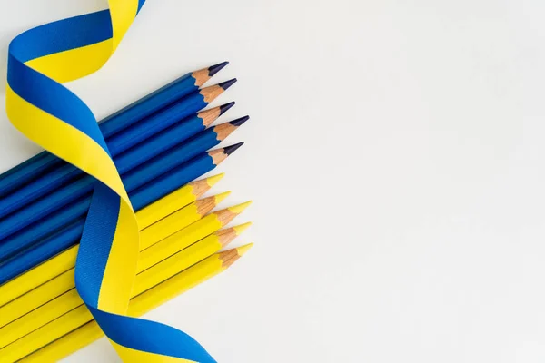 Top view of blue and yellow ribbon on color pencils on white background — Stock Photo