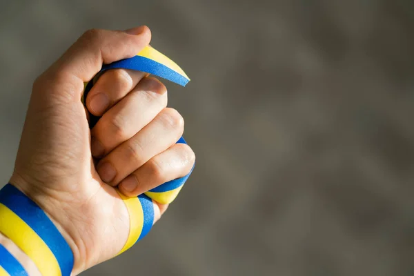 Cropped view of man holding blue and yellow ribbon on grey background — Stock Photo