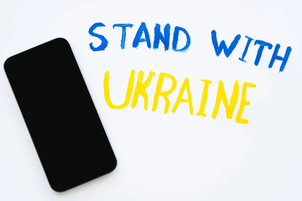 Ansicht des Smartphones in der Nähe gemalten Ständer mit ukrainischen Schriftzug auf weißem Hintergrund — Stockfoto