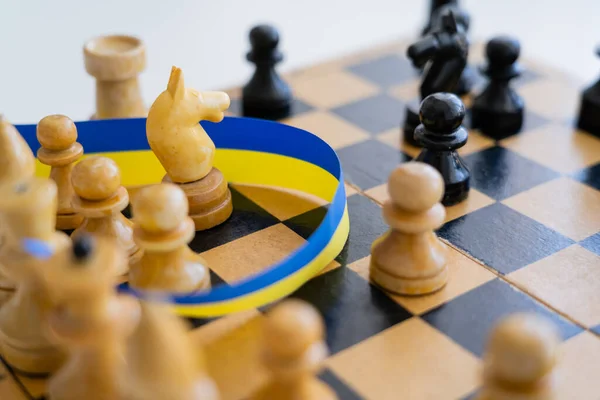 Vista de perto da fita azul e amarela perto de figuras de xadrez a bordo isoladas em branco — Fotografia de Stock