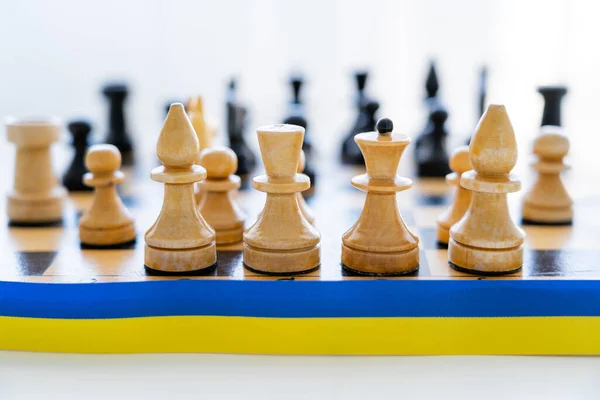 Close up view of blue and yellow ribbon near chess on chessboard on white background — Stock Photo